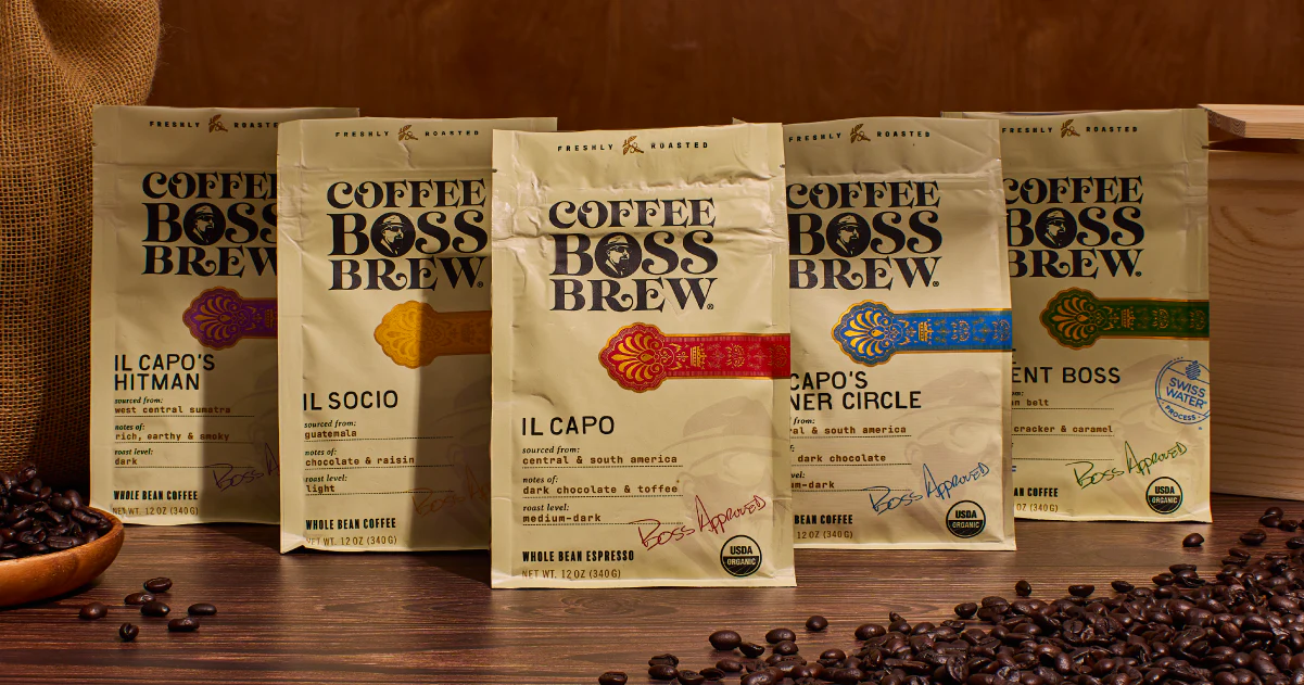 Five Coffee Boss Brew blends — Hitman, Il Socio, Il Capo, Inner Circle, and The Silent Boss on a dark wood surface with scattered beans